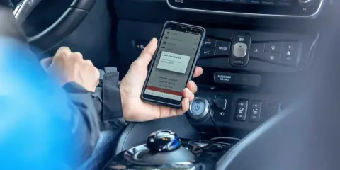 Mano che tiene uno smartphone con app di navigazione attiva, mostrando il **power cruise control** per un viaggio in auto.