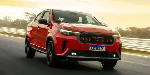 La Fiat Fastback 2026 rossa sfreccia su una pista, con il sole che illumina il cielo.