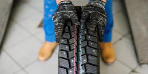 Mani guantate esaminano un battistrada usurato, un segno per capire se le gomme sono da cambiare.