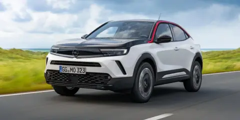 Opel Mokka bianco e nero con tetto rosso, su strada panoramica. Nonostante il design accattivante, alcuni utenti segnalano opel mokka difetti.