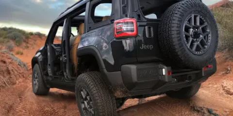 Un fuoristrada elettrico Jeep nero affronta un sentiero sterrato nel deserto, con le portiere aperte e una ruota di scorta sul retro.