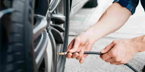 Mani che gonfiano uno pneumatico. Evitare pneumatici troppo gonfi conseguenze: usura irregolare e minore aderenza.