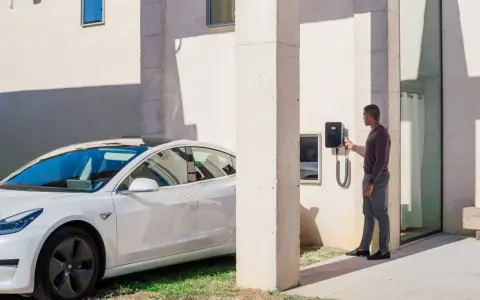 Uomo accanto a un'auto elettrica bianca, che interagisce con una wallbox V2C. Un bonus per la ricarica intelligente.
