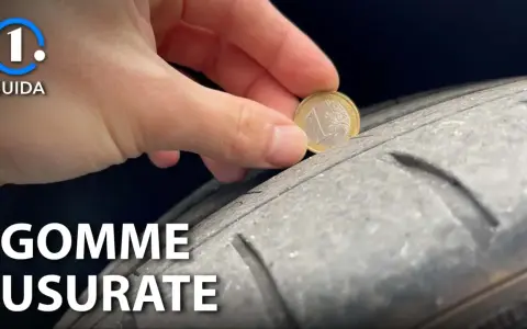 Una mano inserisce una moneta da 1 euro in un solco di uno pneumatico per mostrare come vedere se le gomme sono consumate.