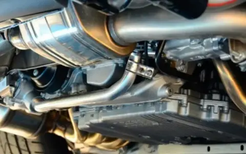 Dettaglio del sistema di scarico di un'auto, con il tubo di scappamento auto lucido e altri componenti metallici.