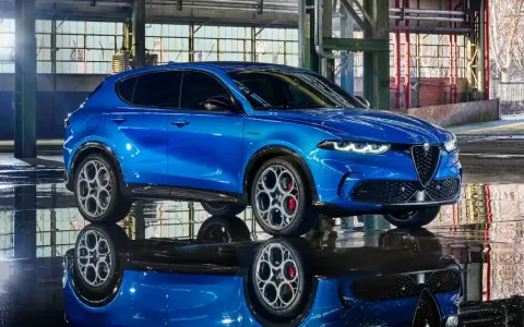 Alfa Romeo Tonale blu, un esempio di stellantis auto elettriche, riflette sul pavimento bagnato di un capannone industriale.