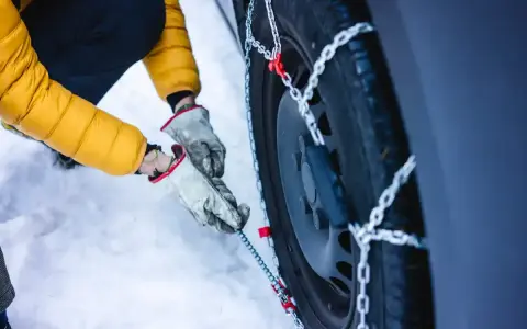 Mani guantate montano le catene da neve su una gomma 4 stagioni. Se ho le gomme 4 stagioni devo avere le catene per la sicurezza invernale.