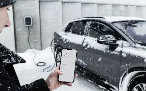 Persona controlla la carica di auto elettriche con lo smartphone, mentre nevica. Il freddo non ferma la tecnologia.