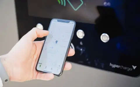 Mano che usa smartphone con mappa per trovare stazione di ricarica. L'app mostra la posizione e le opzioni per monitorare la carica.