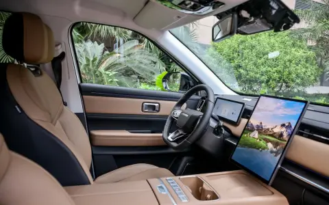 Interni del Jaecoo 7: sedili in pelle beige e nera, volante moderno e un grande schermo centrale con paesaggio montano.