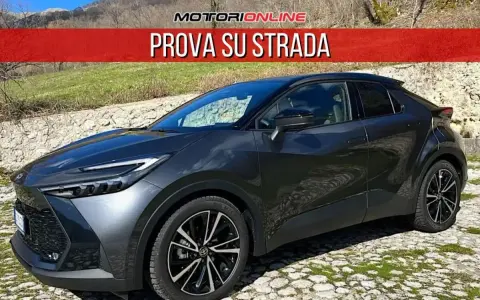 Toyota C-HR grigia parcheggiata su un selciato, con la scritta "PROVA SU STRADA". La sua linea moderna suscita un senso di delusione per chi si aspettava di più.