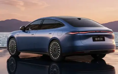 BYD Seal 08, berlina blu elettrica, riflette sull'acqua al tramonto, con montagne sullo sfondo.