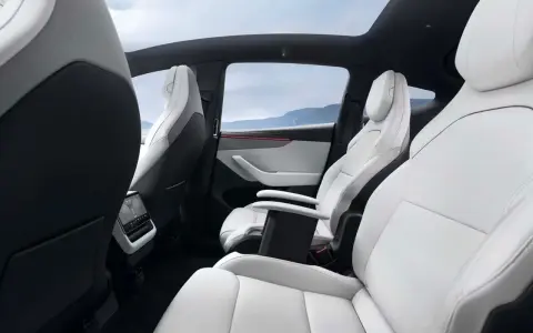 Interni bianchi e neri del Tesla Model Y, con sedili in pelle, tetto panoramico e vista sulle montagne.