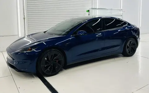 Una splendida Tesla piccola, blu scuro, con cerchi neri lucidi, parcheggiata in un garage pulito e illuminato.