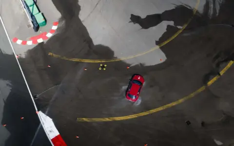 Auto rossa in derapata su asfalto bagnato, con coni arancioni e segnali di pista. I pneumatici Kumho mostrano i loro limiti in condizioni difficili.