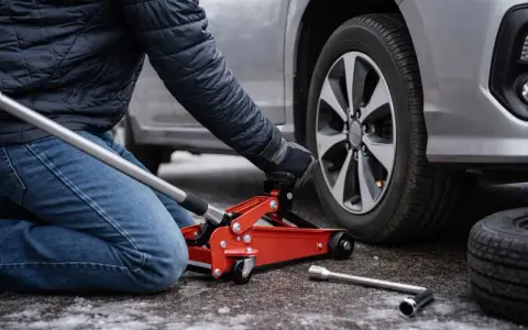 Persona che usa un cric rosso per sollevare un'auto, mostrando dove mettere il cric sotto la macchina per cambiare una gomma.
