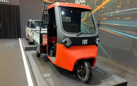 Un vivace Fiat Tris arancione e grigio, un veicolo a tre ruote per il trasporto merci, esposto su una pedana.