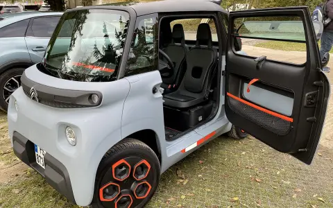 Un'auto elettrica due posti grigia con dettagli arancioni, porte aperte, sedili neri e cerchi distintivi.