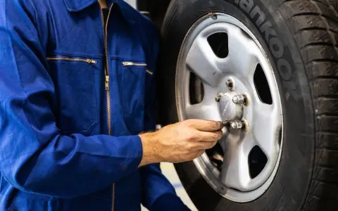 Meccanico in tuta blu controlla i bulloni di una ruota. Ci si chiede dopo quanti km si cambiano le gomme per sicurezza.