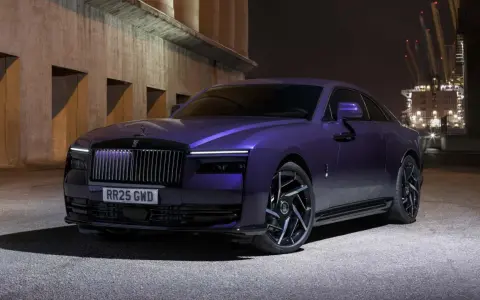 Una Rolls-Royce sportiva viola metallizzato, con un design audace e cerchi neri, parcheggiata di notte vicino a un porto industriale.