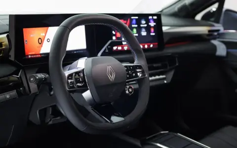 Volante e cruscotto digitale con schermi moderni, dettagli blu e logo Renault. Interni della nuova Clio 2026.