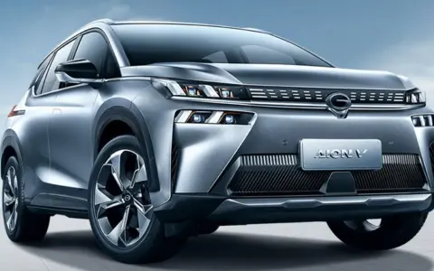 Un SUV grigio metallizzato, l'Aion V, con un design moderno e fari a LED affilati, si presenta su uno sfondo blu cielo.