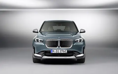 La BMW iX1, con la sua impressionante autonomia, si presenta frontalmente in un ambiente minimalista.