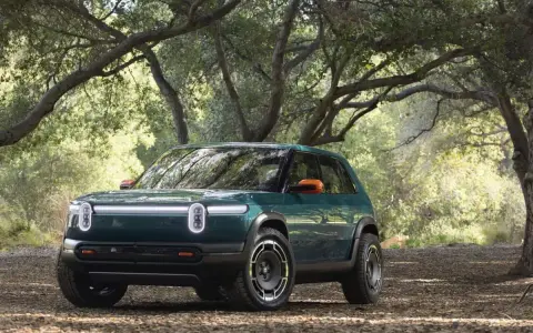 Un'avventura elettrica ti aspetta con la **Rivian R3X** verde bosco, pronta ad affrontare sentieri tra gli alberi.