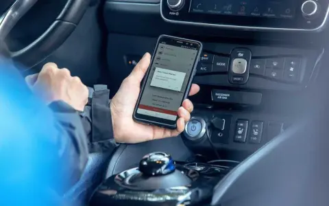 Mano che tiene uno smartphone con app di navigazione attiva, mostrando il **power cruise control** per un viaggio in auto.