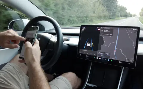 Mani sul volante, ma lo sguardo è sullo smartphone mentre il **Tesla Autopilot** guida. Navigazione e musica sul grande schermo.