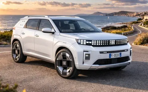 Un'imponente Fiat, quasi un giga panda, sfreccia su una strada costiera al tramonto.