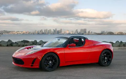Tesla Roadster rosso fiammante, con la silhouette di una città all'orizzonte.