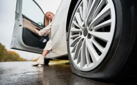 Donna esce dall'auto con gomme sgonfie sul bagnato.