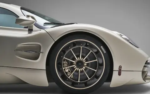 Dettaglio di un'auto sportiva color champagne, con focus sul montaggio pneumatici e cerchi in lega dorati.