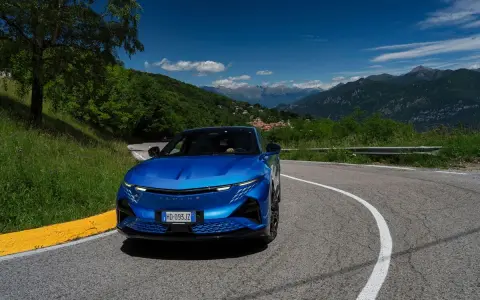 L'Alpine A290 sfreccia su una strada di montagna panoramica, con un cielo azzurro e montagne sullo sfondo.