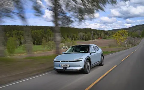 La Hyundai Ioniq 5 sfreccia su una strada panoramica tra alberi e colline verdi, con un cielo nuvoloso.