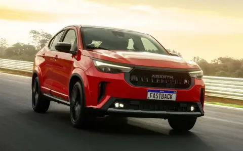 La Fiat Fastback 2026 rossa sfreccia su una pista, con il sole che illumina il cielo.