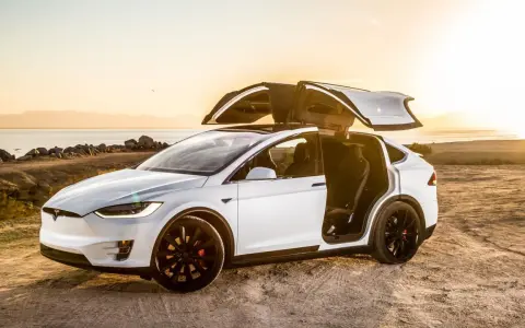 Tesla Model X bianca con portiere ad ali di gabbiano aperte al tramonto, un'auto elettrica che rappresenta il lusso e l'innovazione, forse la tesla più costosa.