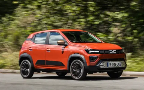 Dacia Spring arancione in movimento, la sua compatta lunghezza la rende ideale per la città.