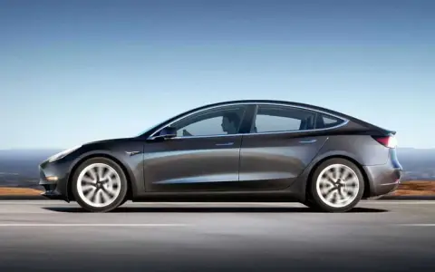 Tesla grigia in movimento su strada, con un conducente al volante. Quanti km fa una Tesla? Dipende dal modello e dalla batteria.