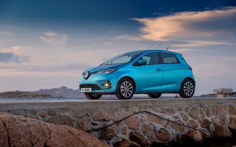 Un'elegante Renault Zoe blu, uno dei tanti modelli Renault, è parcheggiata su un muretto di pietra con il mare e le montagne sullo sfondo.