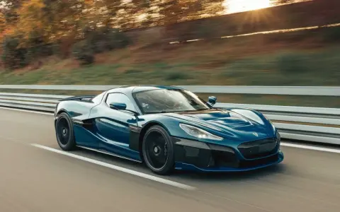 La **auto elettrica più veloce** sfreccia su una strada, con il sole che tramonta tra gli alberi sullo sfondo.