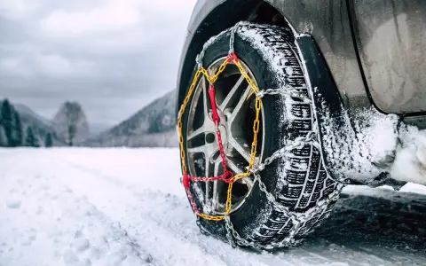 Catene da neve senza codice: come riconoscerle. Ruota di un'auto con catene montate su strada innevata.