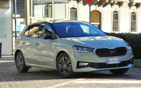 A light green Skoda Fabia hatchback with a black roof is parked on a cobblestone street in front of a building.