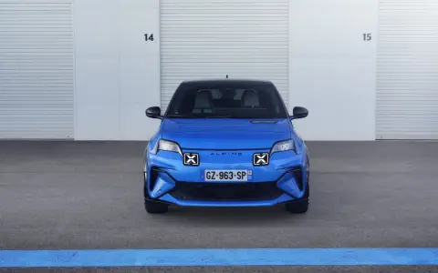 La nuova Alpine A290, un'auto elettrica sportiva blu brillante, attende il suo momento davanti a un garage con porte chiuse.