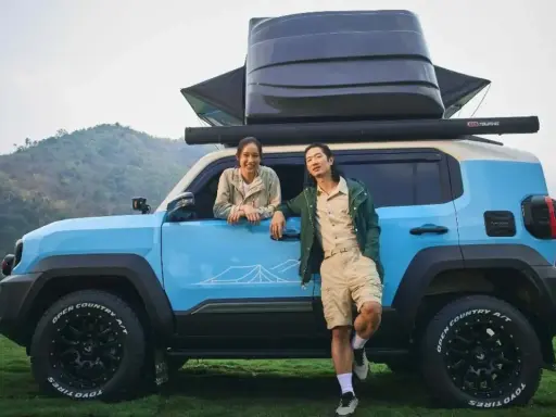 Coppia sorridente accanto a un toyota land cruiser mini blu, pronto per l'avventura con tettoia e box sul tetto.