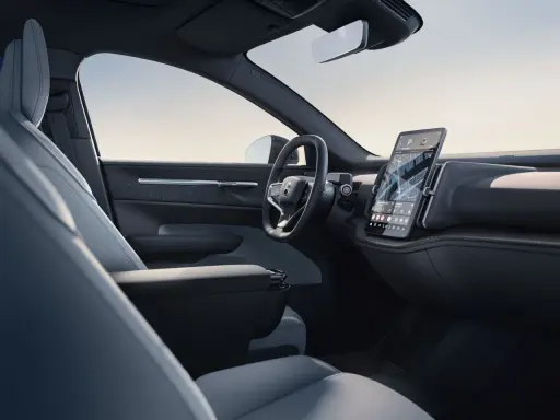 Interni minimalisti del Volvo EX30: sedili chiari, volante moderno e grande schermo centrale con navigazione.