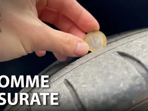 Una mano inserisce una moneta da 1 euro in un solco di uno pneumatico per mostrare come vedere se le gomme sono consumate.