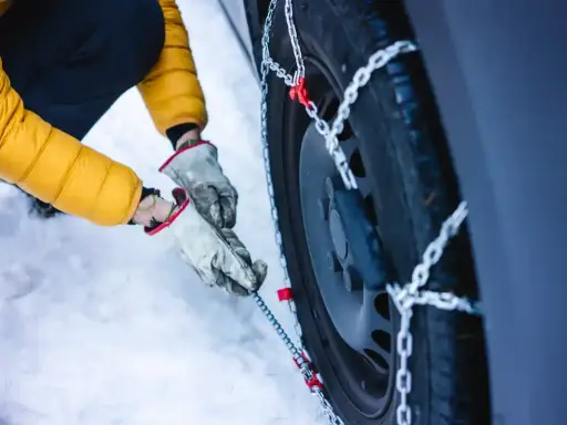 Mani guantate montano le catene da neve su una gomma 4 stagioni. Se ho le gomme 4 stagioni devo avere le catene per la sicurezza invernale.