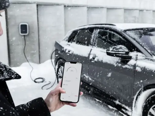 Persona controlla la carica di auto elettriche con lo smartphone, mentre nevica. Il freddo non ferma la tecnologia.